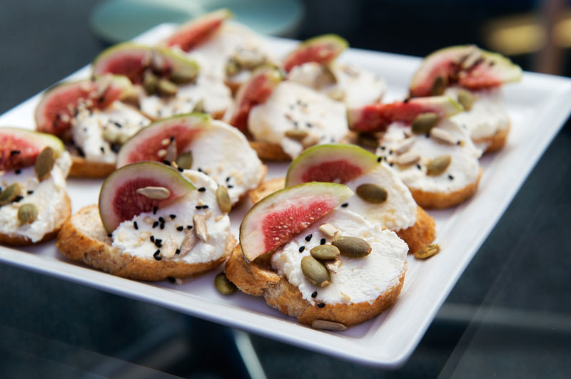 A plate of snacks which appear to be fig, seeds and goats cheese on a crisp bread